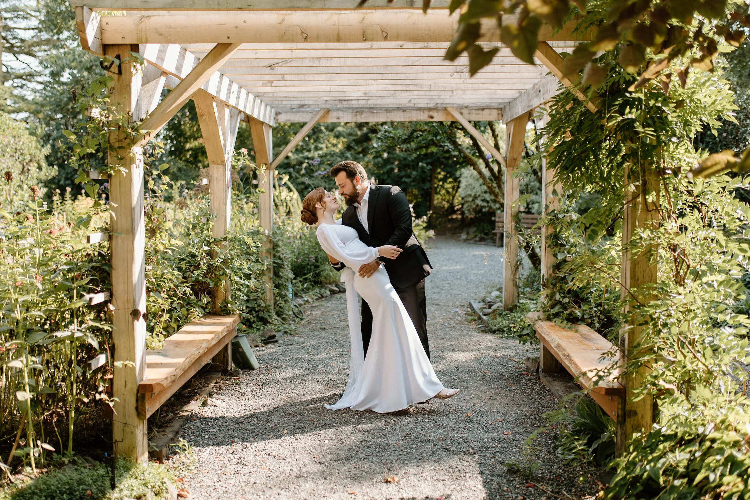 A bride and groom kissing beneath a garden arbor